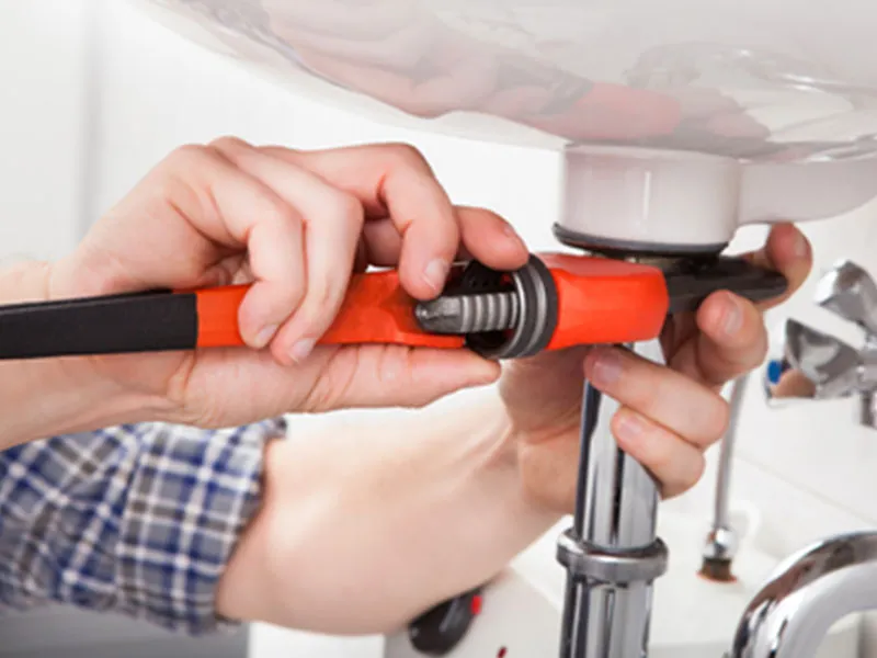 A man using a wrench to repair a sink, demonstrating practical plumbing skills and home maintenance.