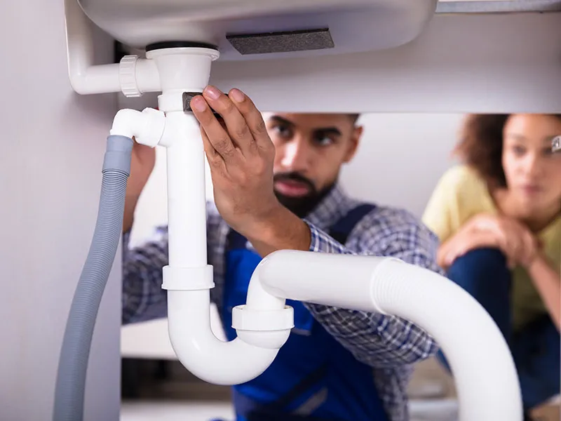 A man and woman are collaboratively repairing a sink drain in a home setting, demonstrating teamwork and problem-solving skills.