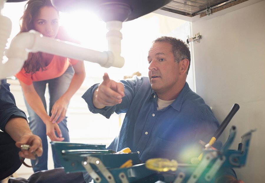 A man and woman working on a sink, providing plumbing services.