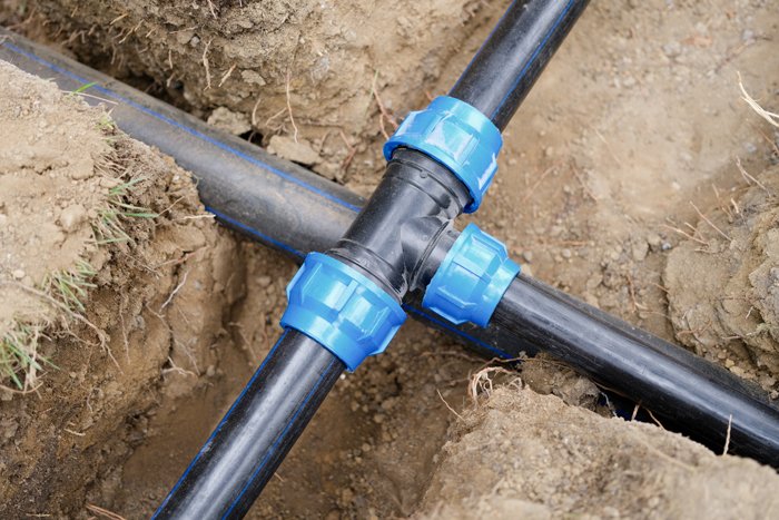 A PVC pipe is positioned in the ground, with a hose nearby, illustrating a typical plumbing installation.