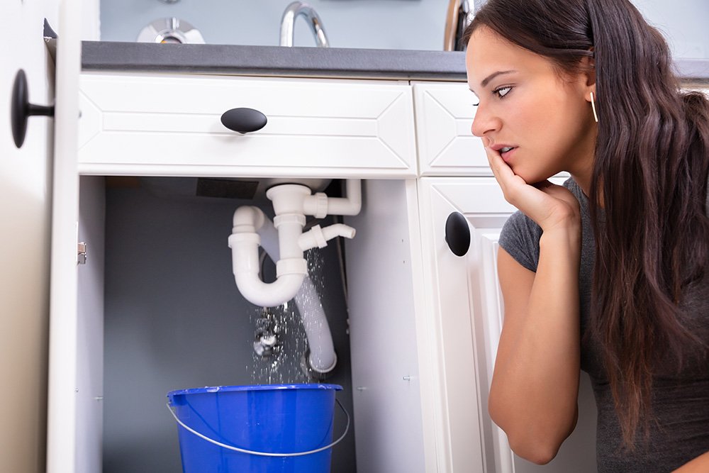 Woman checking sink with bucket for plumbing issue