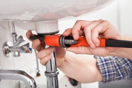 A man using a wrench to repair a sink, demonstrating practical plumbing skills and home maintenance.