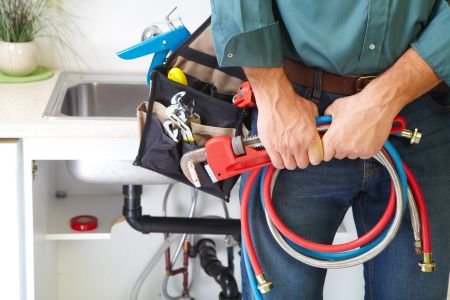 A plumber stands confidently, holding a hose and tools, ready to tackle any plumbing challenge.