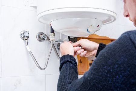 A man repairing a water heater in a kitchen.