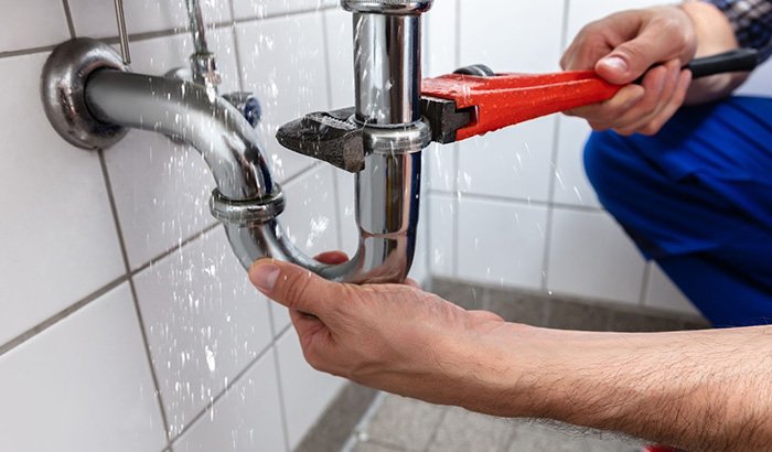 A man using a wrench to fix a pipe, addressing plumbing problems like a leaky faucet caused by hard water