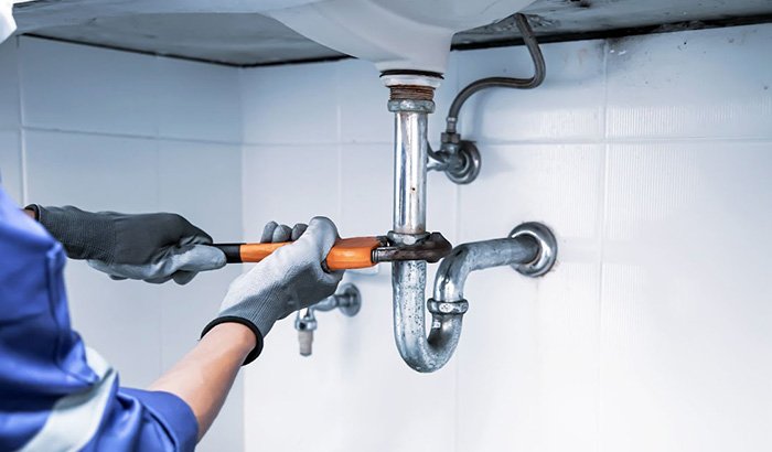 A plumber from a local plumbing service fixing a pipe in a bathroom for plumbing leak repairs.