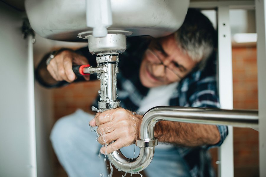 A man repairing a sink faucet, focused on the task with tools in hand, demonstrating home maintenance skills.